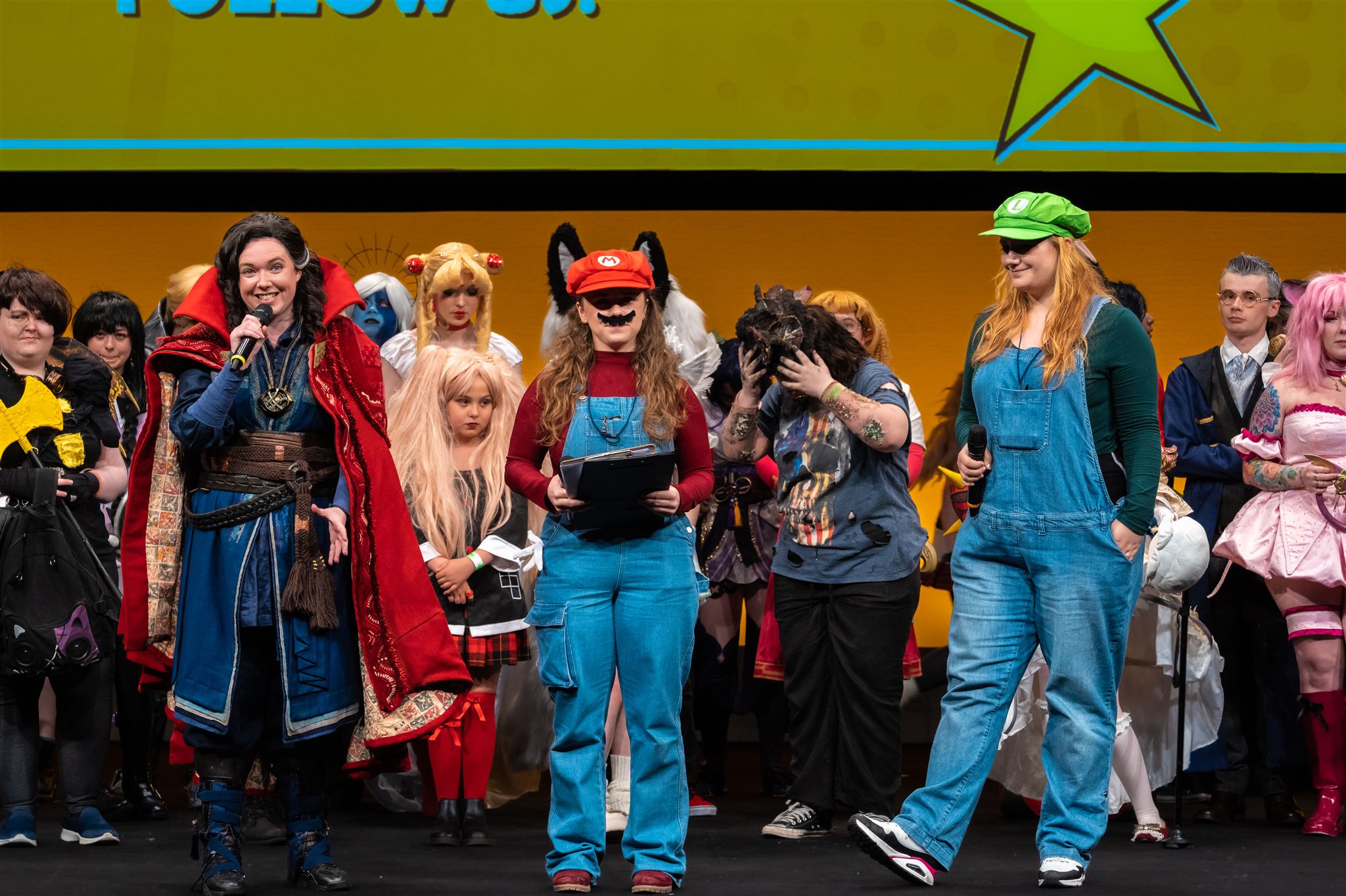 Captain Amelia, Unfortunate Jinx, and Perfect Musix are three white women holding microphones and clipboards. They are dressed as Doctor Strange, Mario, and Luigi.